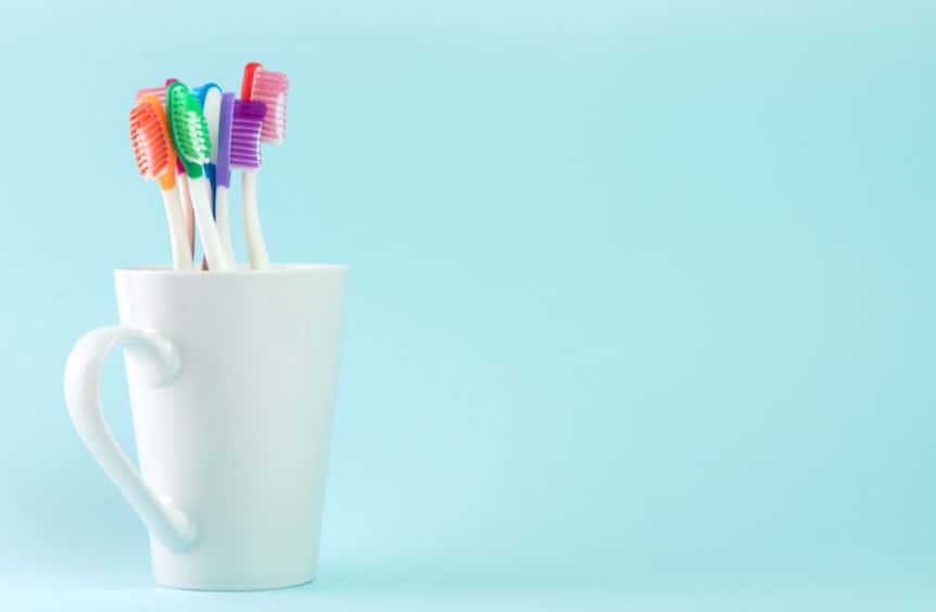 Multicolor toothbrushes in white mug, with copyspace