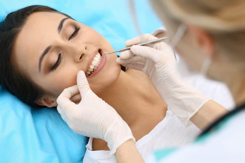 Young female patient visiting dentist office.Beautiful woman with healthy straight white teeth sitting at dental chair with open mouth during oral checkup while doctor working at teeth. Dental clinic, stomatology concept